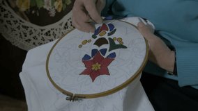 Embroidery by pattern, tying knot to finished part of doily. Woman making flower design on textile with needle and thread, close up. Lady embroidering decoration on tablecloth, craft, hobby, raw video