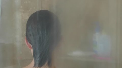 A dolly shot of a beautiful woman in a glass and tile shower washing her long hair