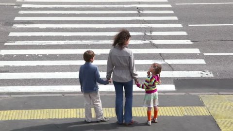 Mother and her two children, boy and girl, cross road at pedestrian crossing after car drove and other stopped to let them pass, then cars ride