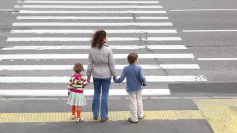 Mother and her two children, boy and girl, cross road at pedestrian crossing, after all cars passed