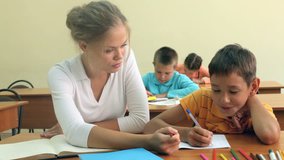 Young teacher sitting by her pupil and helping him 