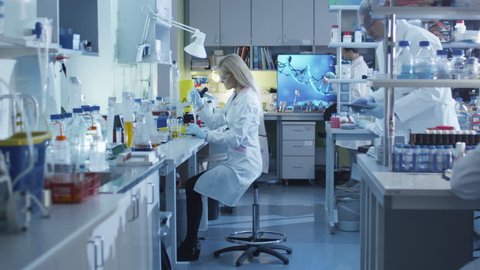Female scientist is using a micro pipette while working in a laboratory with colleagues. Shot on RED Cinema Camera in 4K (UHD).