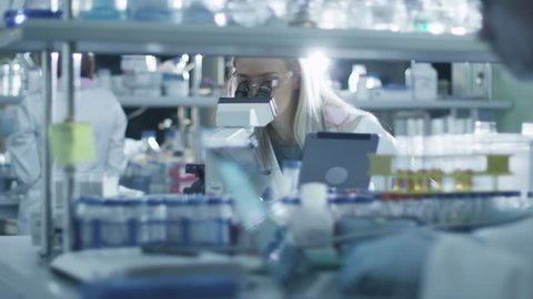 Female scientist is using a microscope and a tablet while working in a laboratory. Shot on RED Cinema Camera in 4K (UHD).