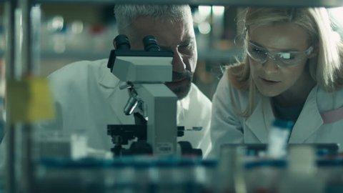 Male and female scientist are working with a microscope and a tablet in a laboratory. Shot on RED Cinema Camera in 4K (UHD).