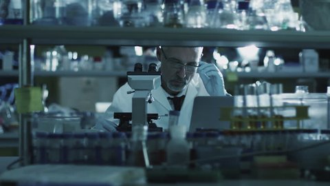 Tired senior male scientist is working with a microscope in a laboratory. Shot on RED Cinema Camera in 4K (UHD).