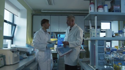Senior scientist is walking with documents in a laboratory where colleagues are working.  Shot on RED Cinema Camera in 4K (UHD).