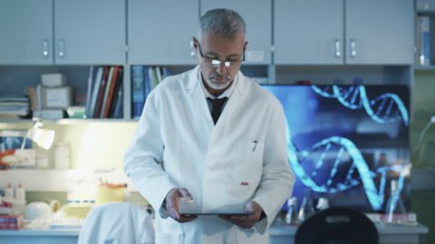 Senior scientist is walking with a tablet in a laboratory where colleagues are working.  Shot on RED Cinema Camera in 4K (UHD).
