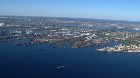Aerial: Bayonne New Jersey piers along New York Harbor on a clear blue day. Ships dock and unload goods for trucking across America (New York - 2015)