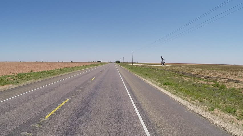 Point of view vehicle driving shot of a West Texas highway. A driver's viewpoint of the roadway and oil wells and oil jacks in the fields passing by.