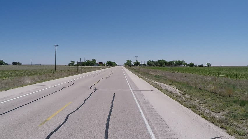 Point of view vehicle driving shot on a West Texas highway. A traveler commutes toward a farm or ranch along the roadway in rural area.