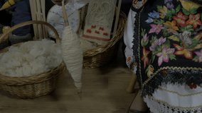 Spinning wool with spindle, pan right, close up, in background basket with wool, making yarn in workshop. Performing old crafts or hobby on old traditional way, holding hands, raw video, slow motion