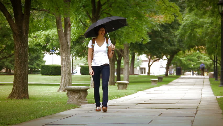 A student shares her umbrella on a college campus while walking to class.