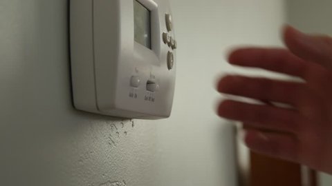 A dolly shot of a man turning up and down the temperature on a thermostat in a home