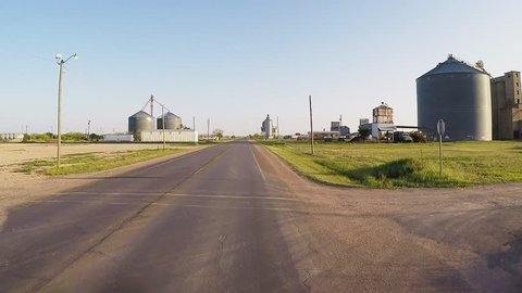 CROWELL, TX/USA - August 3, 2015: POV driving by a modern farm at sunset. A driver's point of view passing grain silos and other farm related equipment and agricultural buildings.