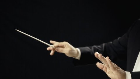The moving hands of an orchestra conductor directing the musicians. Close-up shot. Conducting: directing a musical performance with visible gestures.

