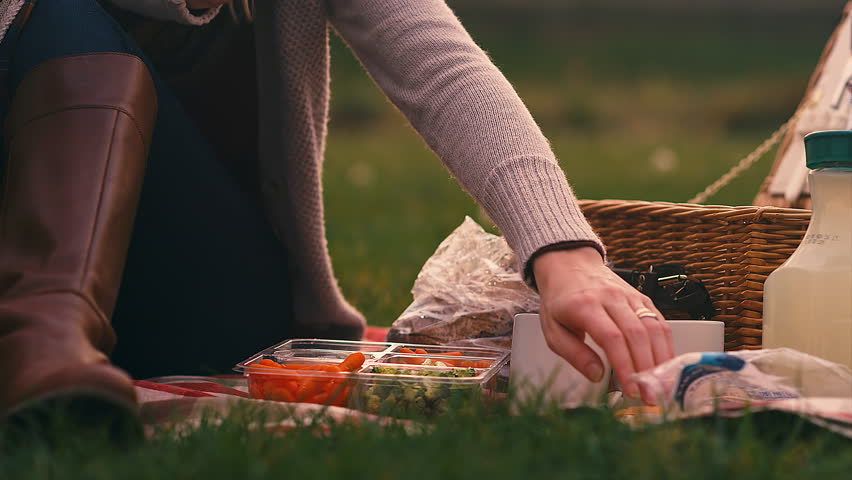Close up of a young woman picking up food at a picnic on a fall day, slow motion