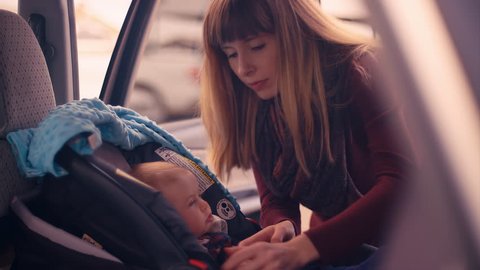 A young mother unbuckling her baby daughter from her car seat