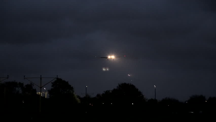 plane flys low into land at heathrow airport london with lens flare of light from plane light as flying over Royalty-Free Stock Footage #13131581