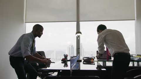 Business people doing a competition and playing a ping pong match in modern office, with sight of city and skyscrapers in background. Wide shot on dolly