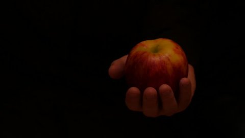 isolated hand with apple moves on black background slow motion