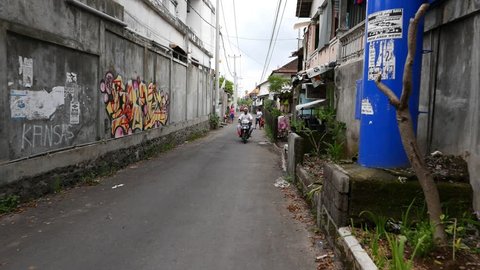 KUTA, INDONESIA - MARCH 12, 2015: Walk through narrow alley, slum area, unidentified people on way, man on scooter, woman with child come towards. Dusk time, urban bystreet, Jalan Margapadmayana
