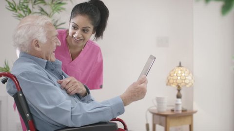 4K Caring young home support nurse helping elderly gentleman to use a computer tablet. Shot on RED Epic