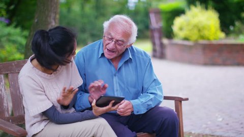 4K Caring young home support worker showing elderly gentleman how to use a computer tablet. Shot on RED Epic