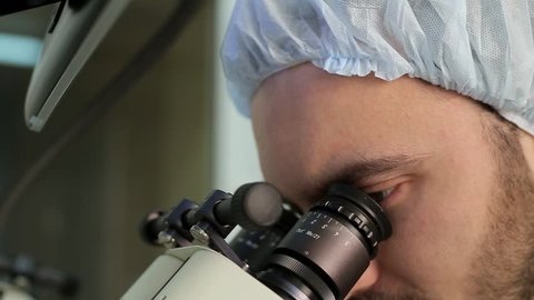 eyes of bearded doctor loking at  eyepieces of microscope system in a medical laboratory Video Stok