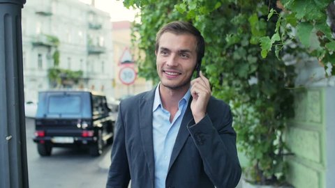 The man walks around the city and speaks by phone. The guy likes conversation therefore he smiles. In slow motion
