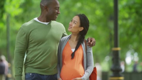 4K Happy mixed ethnicity couple expecting a baby, taking a walk in the park. Shot on RED Epic.