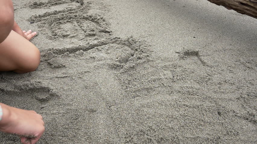 Girl draws a heart in the sand next to "summer" in sand then smiles at camera at Deception Pass State Park beach. 