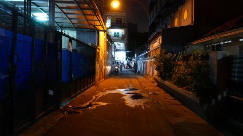 JAKARTA, INDONESIA - MARCH 10, 2015: Dark alley, night urban street, boy on motorbike with phone, man walk aside. POV move along dark bystreet in Kebon Kacang district. Local residents on way.