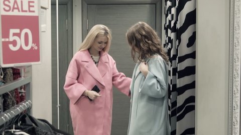 Two girls try on a coat in a locker room in shop