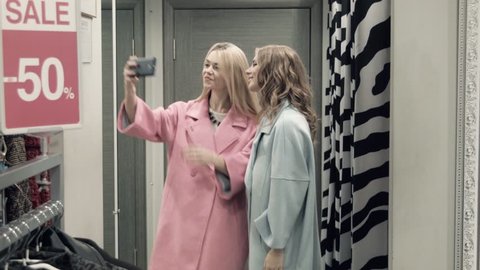 Two girls try on a coat in a locker room in shop