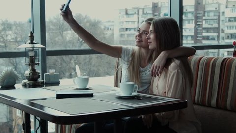 Two girlfriends do selfie in cafe using phone