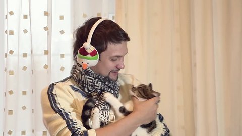 man with headphones in white festive sweater at Christmas and New Year with a cat