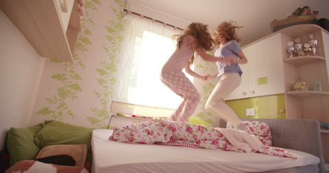 Teen girls who are best friends jumping wildly together holding hands on a bed and wearing pyjamas