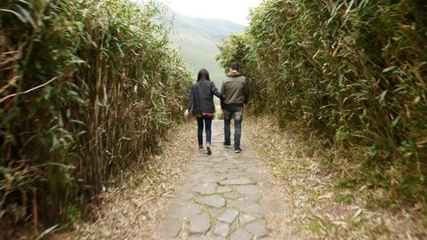TAIPEI, TAIWAN - FEBRUARY 15, 2015: Unidentified young couple come down in green tunnel at high grass tangle, walk downstairs over mountain trail. Camera follow a bit, then stop and show figures