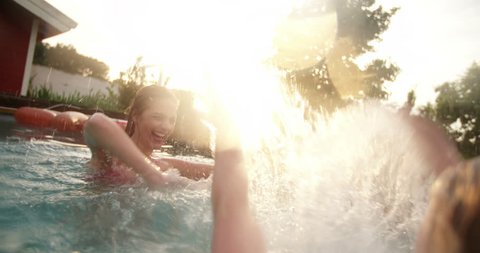 Backyard swimming pool on a late summer evening with girls splashing each other with water while play fighting, with colourful sun flare in Slow Motion