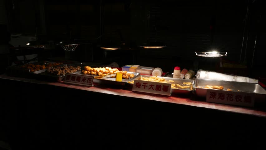 Outdoor bistro at night, table with different frito, traditional snacks in park eatery. Late evening time, darkness around, bright lamp over stall with meals choice on tray, Parallax motion shot