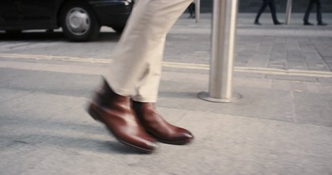 Close crop of businessman feet walking in city. Man commuting to work. Steadicam shot in slow motion with warm natural light on sidewalk