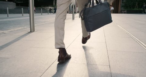 Close crop of businessman feet walking in city. Man commuting to work. Steadicam shot in slow motion with warm natural light on sidewalk