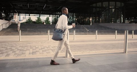 African American Man using business app on smart phone walking in city. Handsome young businessman communicating on smartphone smiling confident. Urban black male professional commuting in his 20s