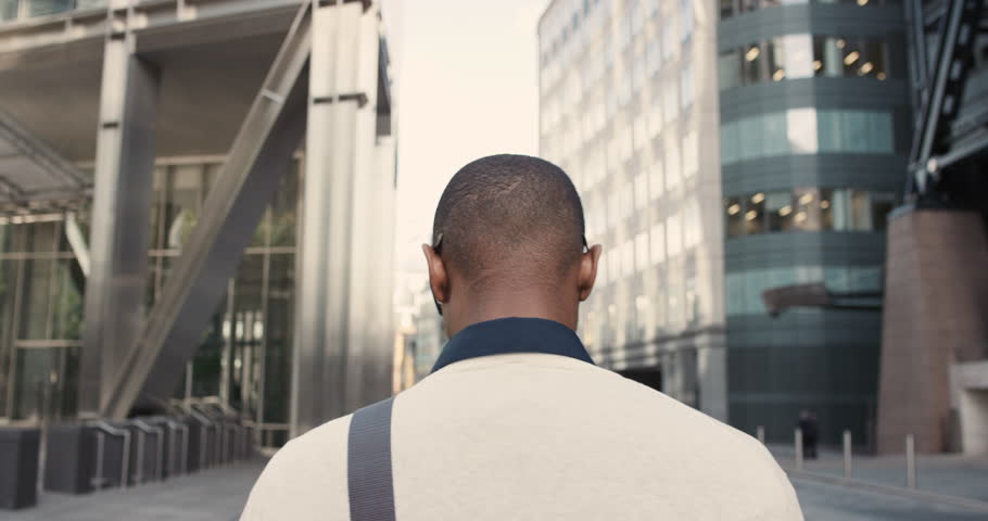 Rear view african american businessman walking in city commuting independently between glass buildings