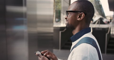 African American Man sms texting using app on smart phone in city. Handsome young businessman using smartphone smiling happy. Urban male professional commuting in his 20s