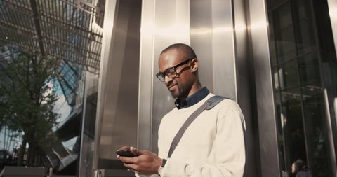 African American Man sms texting using app on smart phone in city. Handsome young businessman using smartphone smiling happy. Urban male professional commuting in his 20s
