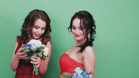 Two beautiful girls with bouquets in the studio. Green background