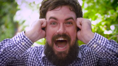 Close up portrait of a young hipster man with a full beard expressing surprise as if he won something such as a prize, or a lottery. 