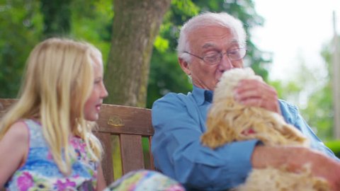 4K Family generations - grandfather & granddaughter chatting as they sit in the garden with pet dog. Shot on RED Epic.