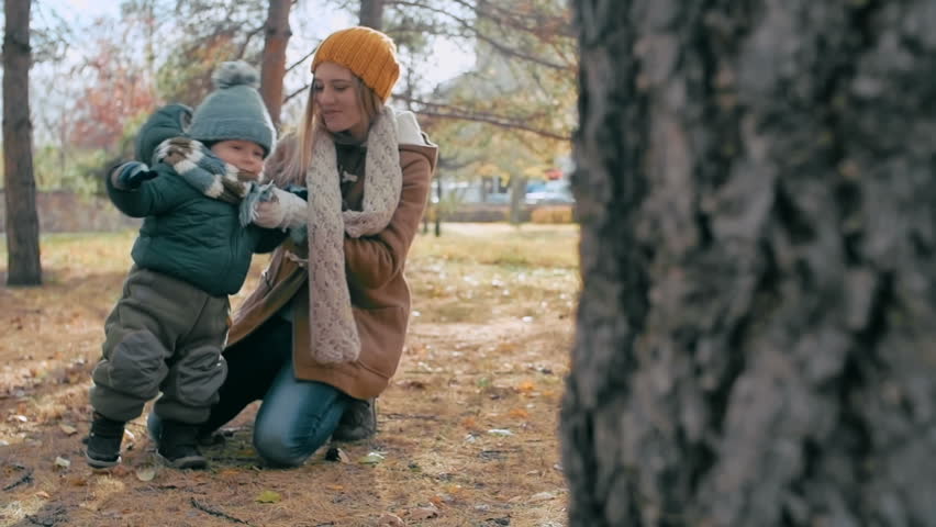 Pretty mother tying her active baby sons knit scarf during a walk in park 